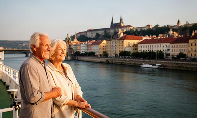 Seniorenpaar an der Reling eines Donau-Flussschiffes mit Blick auf eine europäische Altstadt